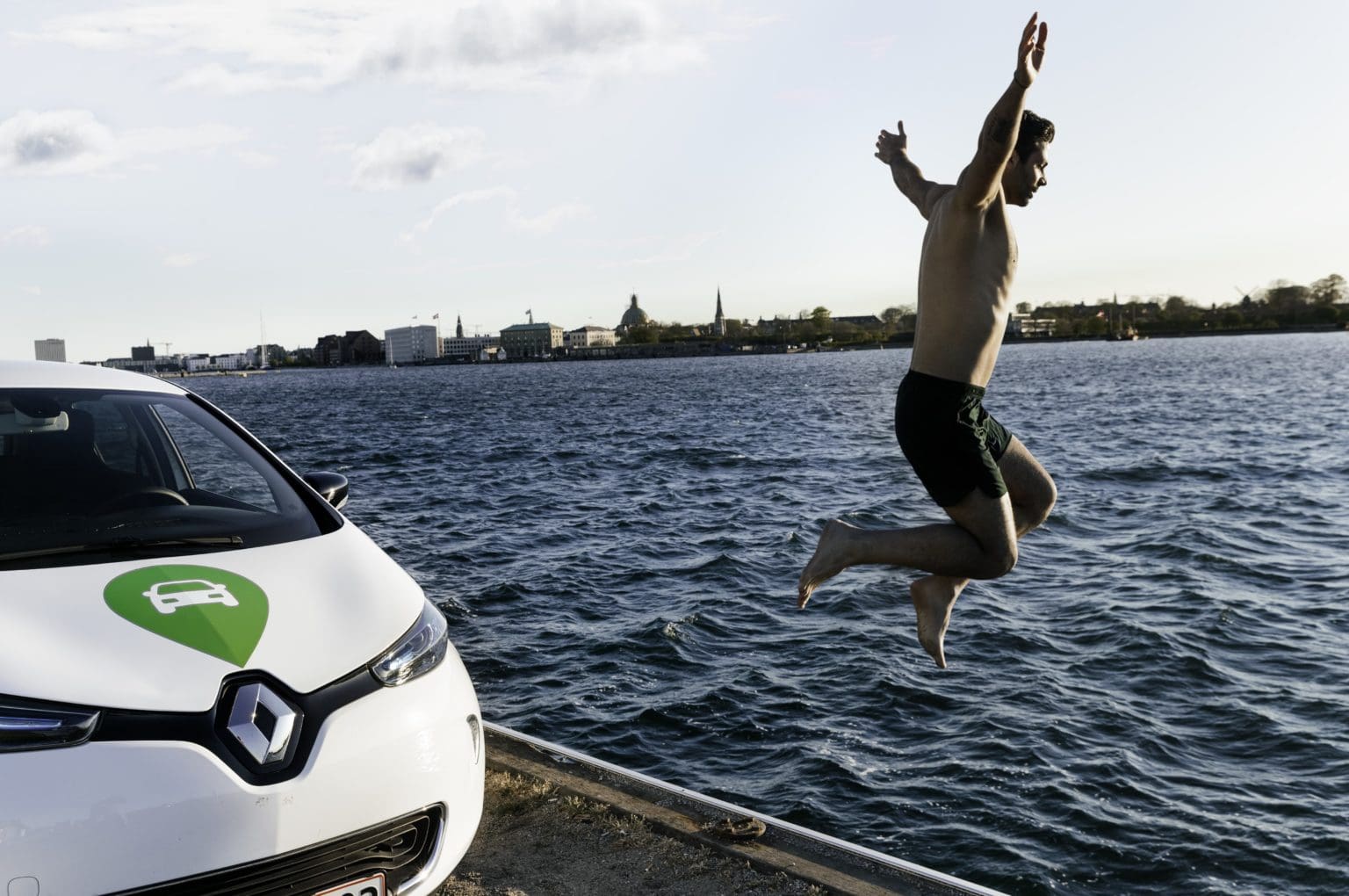 Man jumping in the lake next to a GreenMobility car